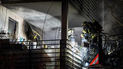 Feuerwehrleute stehen auf einem Balkon, der vom Ruß schwarz geworden ist. 
