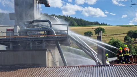 Mehrere Feuerwehrleute spritzen Wasser auf das Dach eines Sägewerks.