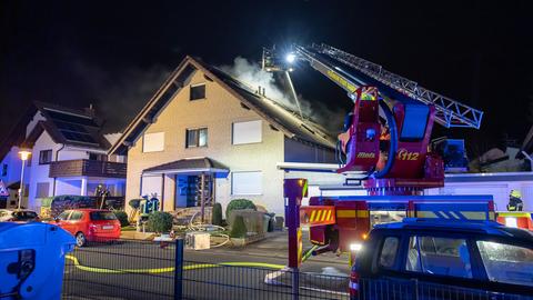 Ein Feuerwehrauto mit Drehleiter steht vor dem qualmenden Haus.