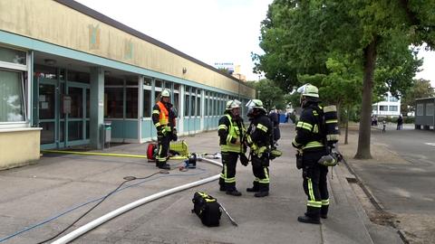 Feuerwehrleute stehen vor einer Schule.