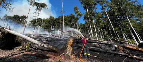 Ein Feuerwehrmann hält einen Schlauch und löscht das Feuer im Taunus.