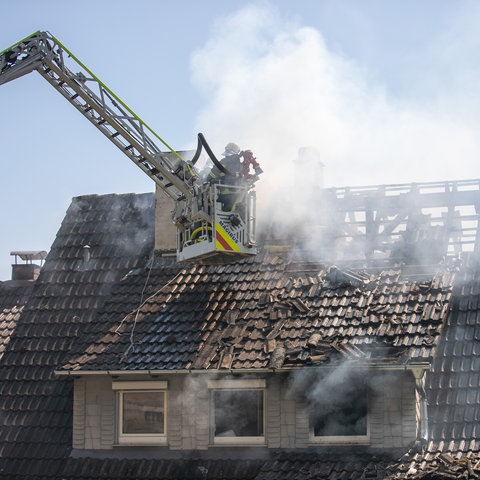 Feuerwehrleute löschen den qualmenden Dachstuhl von einer Drehleiter aus.