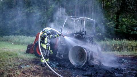 Ein Feuerwehrmann löscht einen ausgebrannten Traktor auf einer Waldlichtung.