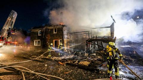 Ein ausgebranntes Haus, davor stehen Feuerwehrleute.