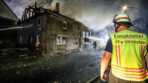 Ein ausgebranntes Haus, davor stehen Feuerwehrleute.