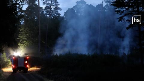 Feuerwehrauto steht im dunklen Wald, daneben Rauchwolken