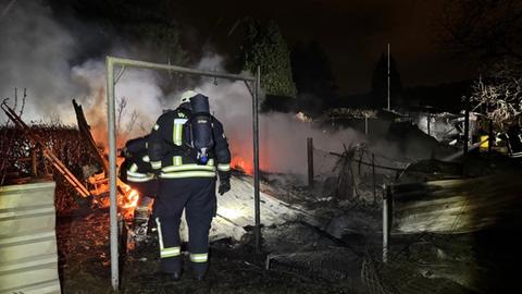 Ein Feuerwehrmann in Schutzausrüstung steht vor dem brennenden Gelände. 