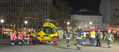 Ein gelber Hubschrauber steht auf dem Kopfsteinpflaster in der Innenstadt, daneben etwa zehn Feuerwehrleute.