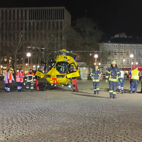 Ein gelber Hubschrauber steht auf dem Kopfsteinpflaster in der Innenstadt, daneben etwa zehn Feuerwehrleute.