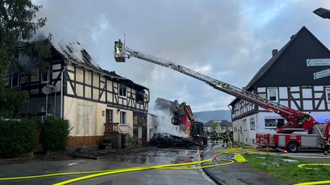 Mit einer Drehleiter löscht die Feuerwehr ein Fachwerkhaus, Rauch steigt aus den Dach auf.