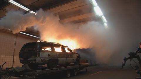 Brennendes Fahrzeugwrack auf Plattform in Tunnel, weißer Rauch