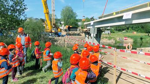 Foto: Kindergartenkinder mit Schutztwesten und roten Helmen stehen vor einer Baustelle.