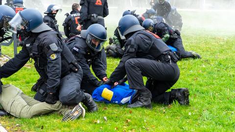 Mehrere Polizisten nehmen gewaltbereite Fußballfans fest. Die Fans liegen am Boden, die Polizisten knieen über ihnen.