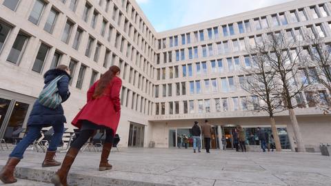 Zwei Studentinnen gehen auf dem Uni-Campus Westend in Frankfurt auf die Eingangstür des Uni-Gebäudes zu.