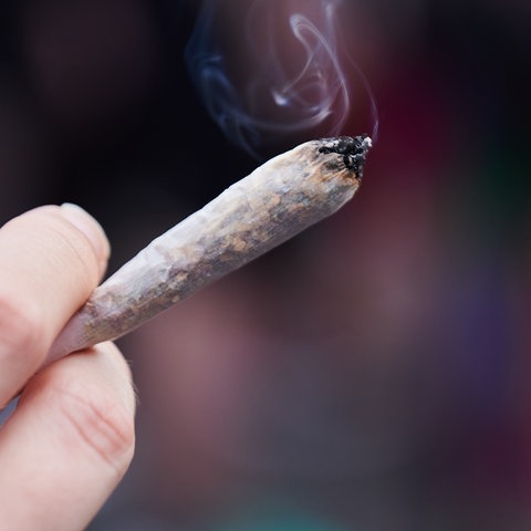 Eine Hand mit einem brennenden Cannabis-Joint. 