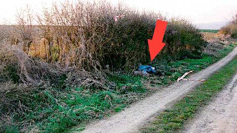 Foto eines Feldwegs in der Landschaft. Am Rand leicht verdeckt ein blauer Müllsack (in dem der Leichnam verborgen war). Ein roter Pfeil markiert in dem Bild die Stelle. 