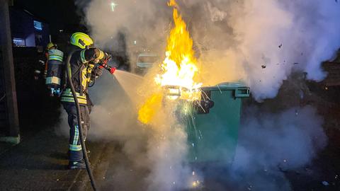 Ein Feuerwehrmann löscht einen brennenden Müllcontainer.