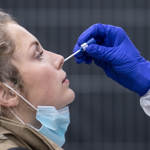 Eine Hand, bekleidet mit Schutzhandschuh, führt ein Teststäbchen in die Nase einer Frau ein.