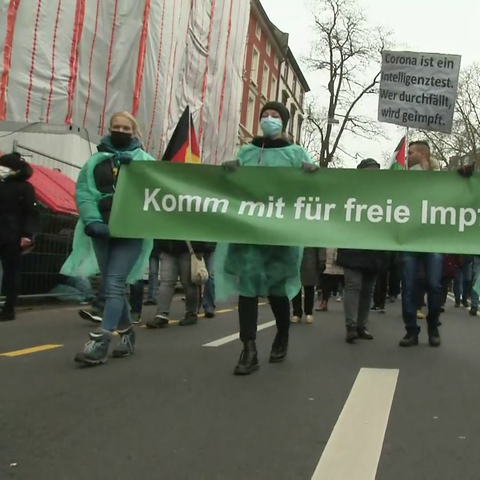 Eine Gruppe von Menschen zieht mit einem Transparent durch eine Straße.