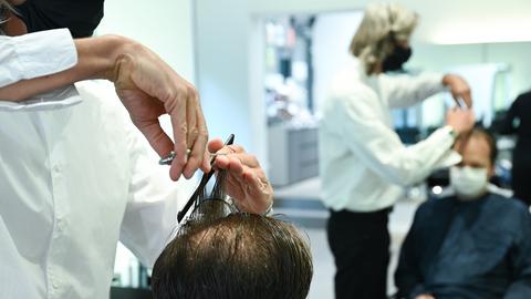 Ein Friseur mit Maske schneidet einem Kunden mit Maske die Haare.