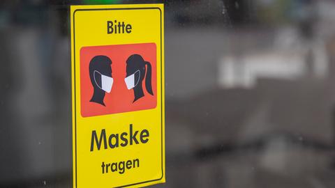 Ein Schild an einer Glastür mit dem Aufruf "Bitte Maske tragen".