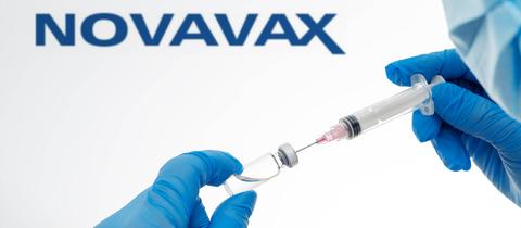 Schriftzug Novavax, davor eine Hand, die mit einer Spritze Flüssigkeit aus einer Ampulle zieht