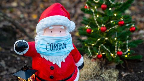 Kleine Weihnachtsmannfigur mit OP-Maske in einem Vorgarten.