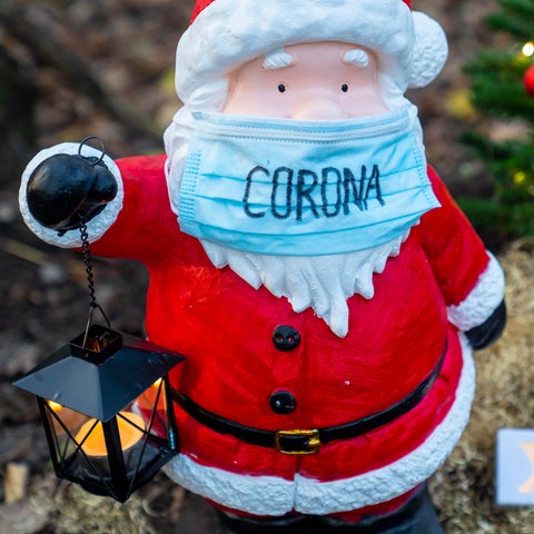 Kleine Weihnachtsmannfigur mit OP-Maske in einem Vorgarten.