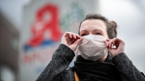 Frau mit Atemschutzmaske vor einer Apotheke