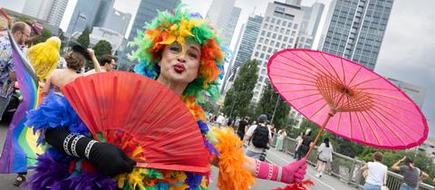 CSD-Teilnehmer im bunten Federboa-Kostüm mit lilafarbenem Schirm - vor der Frankfurter Skyline
