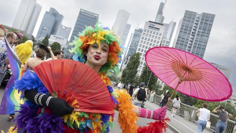CSD-Teilnehmer im bunten Federboa-Kostüm mit lilafarbenem Schirm - vor der Frankfurter Skyline
