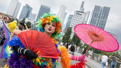 CSD-Teilnehmer im bunten Federboa-Kostüm mit lilafarbenem Schirm - vor der Frankfurter Skyline