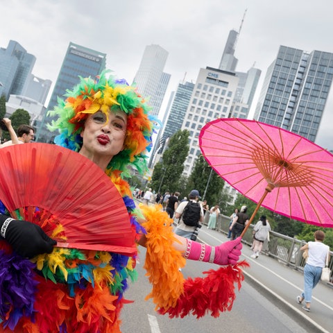 CSD-Teilnehmer im bunten Federboa-Kostüm mit lilafarbenem Schirm - vor der Frankfurter Skyline