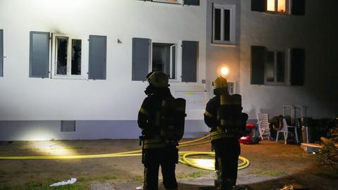 Feuerwehrleute stehen vor einem Haus, am Fenster zeigt sich Ruß
