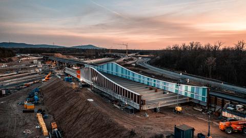 Großbaustelle von oben in der Dämmerung. Ein Teil einer Autobahnbrücke wird über eine Autobahn, die im Bau ist, geschoben.