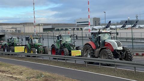 Traktoren fahren am Flughafen-Gelände entlang, im Hintergrund parkende Flugzeuge