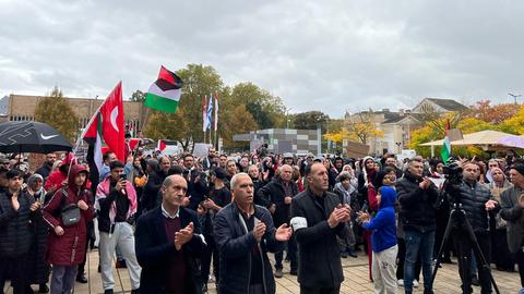 Mehrere Dutzende Menschen stehen vor dem Rathaus in Gießen und schwenken palästinensische und türkische Flaggen. 