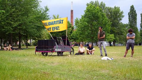 Auf einer grünen Wiese stehen einige Menschen und ein Gefährt mit einem Banner auf dem "Solidarität für Efe" geschrieben steht.