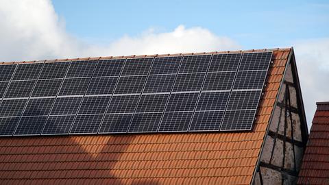 Solar-Module auf einer alten Fachwerk-Scheune. Die Module schimmern im Sonnenlicht, hinter dem Gebäude ziehen große Wolken auf.