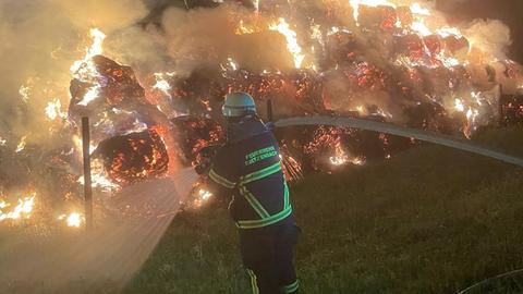 Brennende Heuballen, davor steht ein Feuerwehrmann.