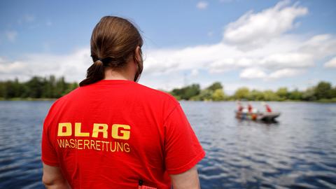 Ein Rettungsschwimmer steht mit dem Rücken zur Kamera vor einem See, DLRG steht auf seinem T-Shirt.