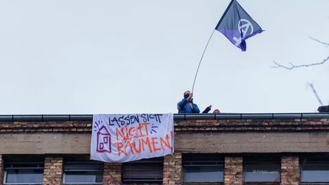 Ein Aktivist steht mit einer Fahne auf dem Dach der Dondorf-Druckerei und schwenkt einen Banner.