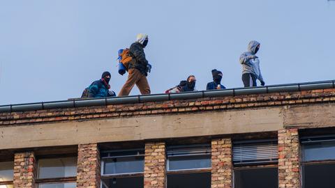 Vermummte Aktivisten stehen auf dem Dach eines Backsteingebäudes.
