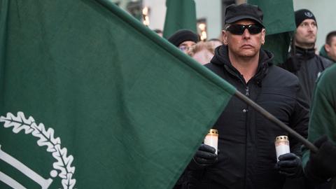 Ein Mann mit zwei Grableuchten in der Hand und einer Fahne des dritten Wegs bei einer Demonstration