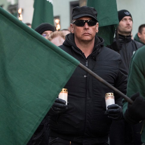 Ein Mann mit zwei Grableuchten in der Hand und einer Fahne des dritten Wegs bei einer Demonstration