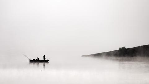 Ein Fischerboot im Frühnebel auf einem See.