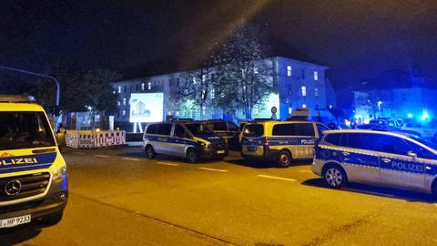 Viele Polizeiautos im Einsatz auf einer Straße vor einem erleuchteten Flüchtlingsheim.