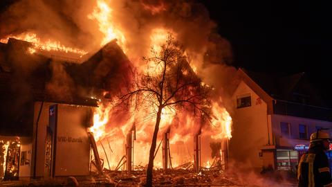 Flammen schlagen aus einem Bankgebäude, davor liegen Trümmer und Splitter