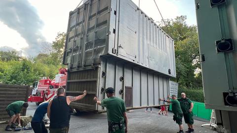 Männer in Arbeitskleidung stehen neben einem großen Transport-Container für Tiere, der an einem Kran hängt.