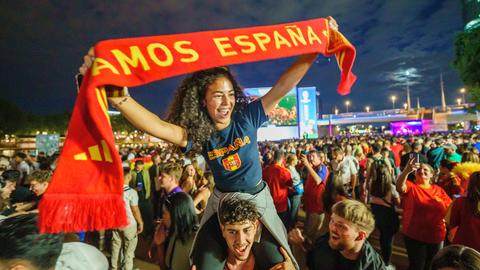 Frau mit Spanien-Schal auf Schultern vor Public-Viewing-Bildschirmen